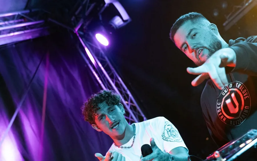 Členové Infinity Vibes DJ za mixážním pultem, jeden s mikrofonem a nášivkou UNIted HK
